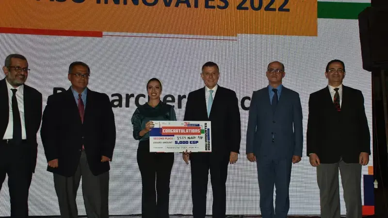 Rania Gamal on the stage receiving award (names and titles at the bottom)